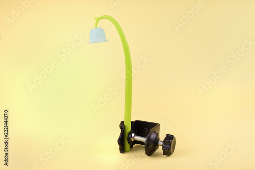 Artificial plastic flower tightened in a metal and plastic desk clamp on a yellow background. Concept of restriction, industrial pressure and environmental control.