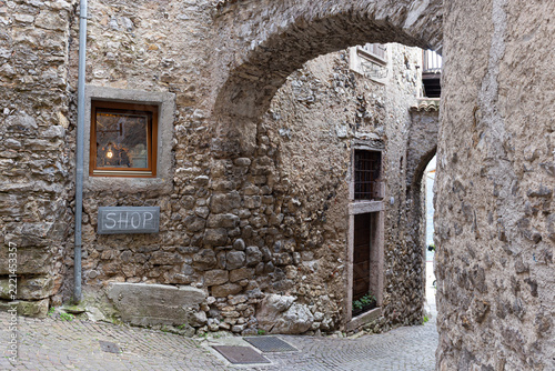 Rustic cobblestone alleyway with artisan shop sign and illuminated window under stone arches in Canale di Tenno medieval village, Italy.