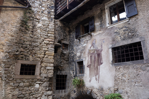 Ancient stone house facade with religious fresco of Saint Anthony the Great and vaulted archways in medieval village of Canale di Tenno, Italy.