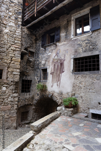 Ancient stone house facade with religious fresco of Saint Anthony the Great and vaulted archways in medieval village of Canale di Tenno, Italy.