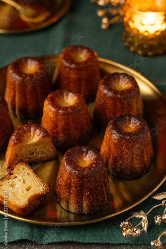 Traditional French canelés dessert on a gold plate and green linen tablecloth. Festive serving. Selective focus.