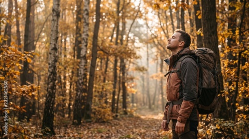 Male hiker with a backpack pausing with eyes closed in a sunlit autumn forest, enjoying a peaceful moment in nature