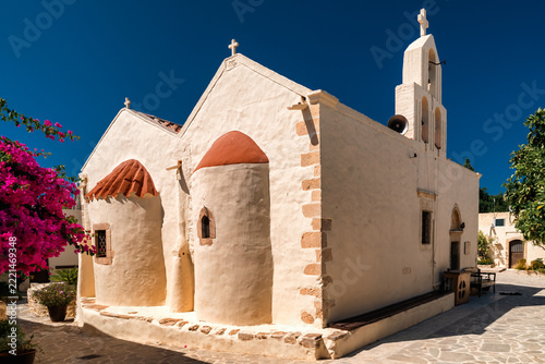 Historic whitewashed church of Panagia Odigitria Monastery with bell tower and pink bougainvillea in Crete, Greece