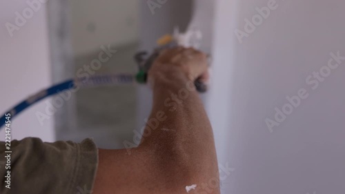 Worker spraying plaster onto interior wall using mechanical spray gun