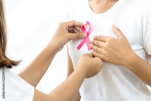 Woman attaching pink ribbon badge on white t-shirt for breast cancer awareness month concept