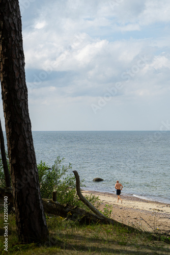 Obraz na plátně Man running along the sandy beach by the sea during a sunny summer day for fitne