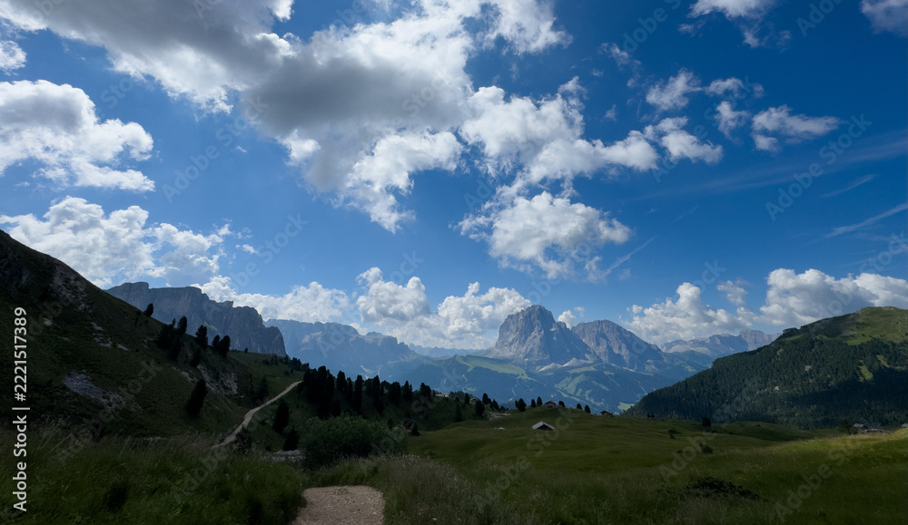 Fototapeta premium View of beautiful landscape in the Alps with fresh green meadows and mountain tops in the background on a sunny day with blue sky and clouds in summertime. Alpe di Cisles, Seceda Ridgeline, Dolomiti ,