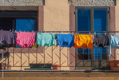 Colorful T-shirts hanging on a balcony, drying in the sun.