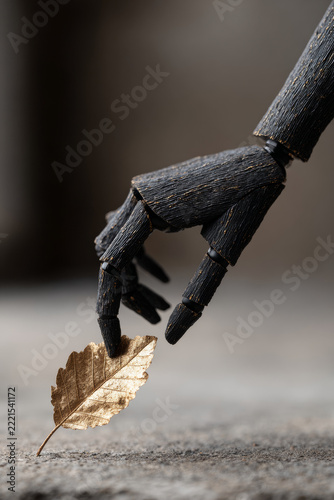 Dark wooden mechanical robot hand touching golden autumn leaf in close-up fine art photography