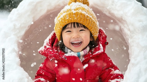 Joyful child in a snowy winter scene smiling from a snow fort with warm clothing and beanie
