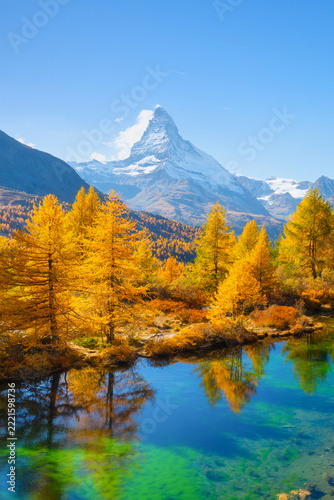 Vertical photo. Matterhorn mountain in Switzerland reflects in a calm alpine lake. Scenic mountain landscape with colorful autumn trees under a clear sky in daytime.