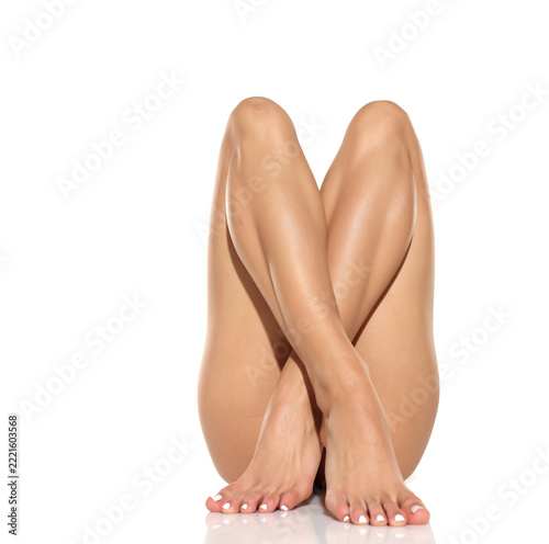 Studio shot of a woman’s legs and feet with smooth depilated skin crossed in an elegant beauty body care pose on a white background.