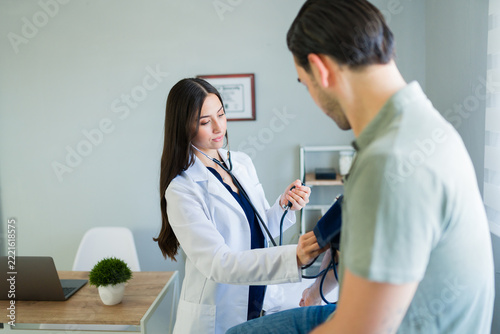 Medical professional checking male patient blood pressure at clinic, young adult man during medical examination