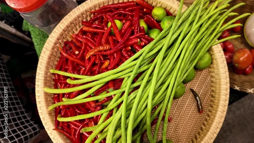 Close up shot of fresh raw ingredients including red chili peppers, long green beans and limes inside a wicker basket at a traditional market stall in Thailand.
