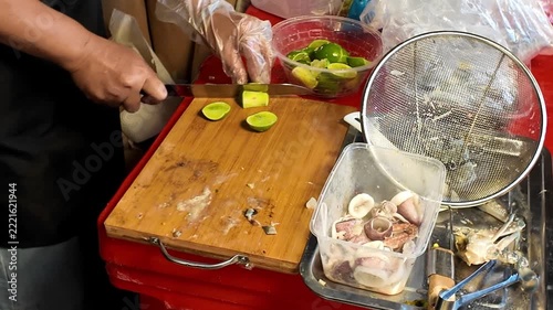Close up shot of street food vendor hands using a knife to slice fresh green limes on a wooden cutting board at a market stall in Thailand.
