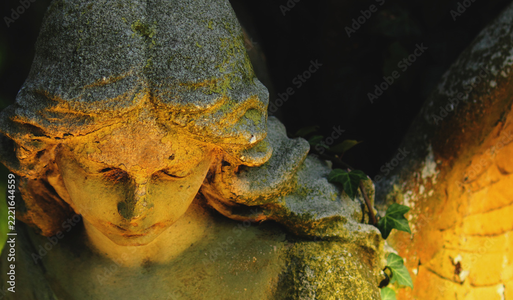 Fototapeta premium Weathered angel statue in warm sunlight, symbolizing grief, compassion, remembrance and hope.