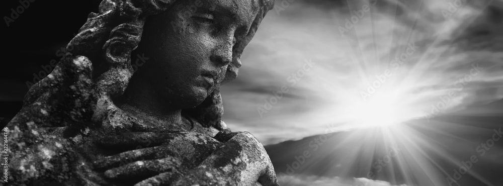 Fototapeta premium Ancient angel statue emerging from darkness toward divine light, symbolizing hope, faith, salvation and the journey of the soul into eternity.