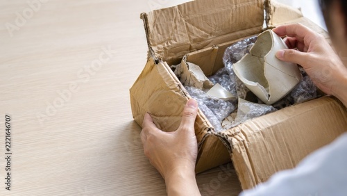 Asian Hands Examining a Crushed Shipping Box with Damaged Contents: A Visual Representation of E-commerce Packaging Failure and the Importance of Quality Control in Online Retail.