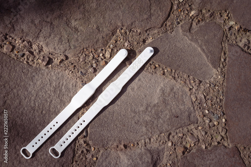 Two White Silicone Identification RFID Wristbands Lying on an Outdoor Stone Pavement Surface
