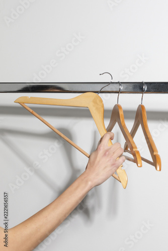 Hand holding a wooden clothes hanger on a metal rail, illustrating clothing selection, wardrobe organization and everyday fashion preparation against a light background.