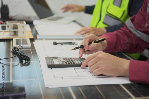 Worker calculating solar panel installation cost with calculator and pencil over technical drawing at desk