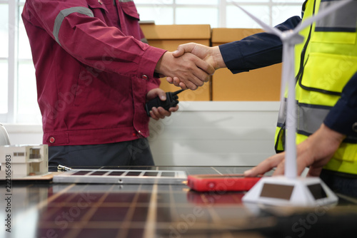Worker handshake, safety vest, solar panel, wind turbine, and cardboard box in renewable energy workspace