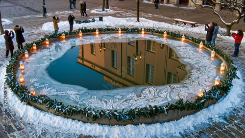 A frozen fountain reflects a warmly lit building