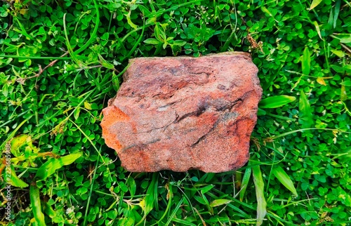 Single red clay brick piece resting on vibrant green grass field in natural daylight background