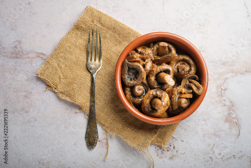 A dish of cooked mushrooms served in a bowl on a piece of burlap, with a fork alongside.