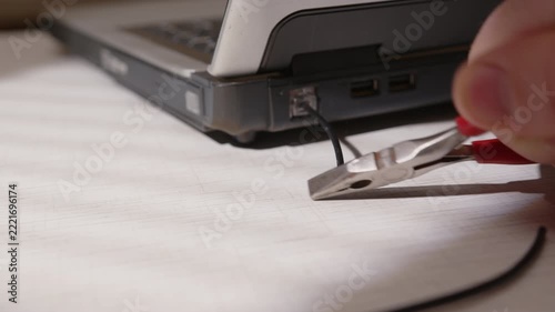 Man's hand cuts internet cable linked to laptop close-up, connection breakdown, communication failure