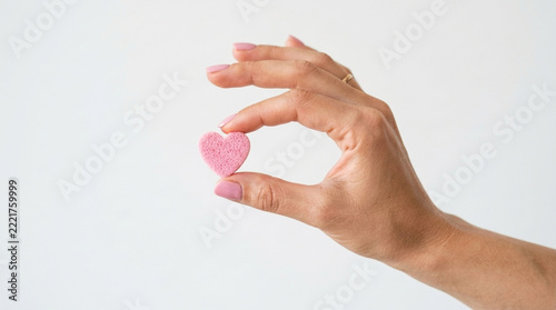 Delicate Pink Heart Held Between Fingertips Against White Background