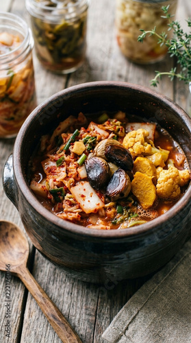 Delicious Kimchi Stew in Ceramic Bowl with Jars Wooden Spoon and Herbs on Rustic Table