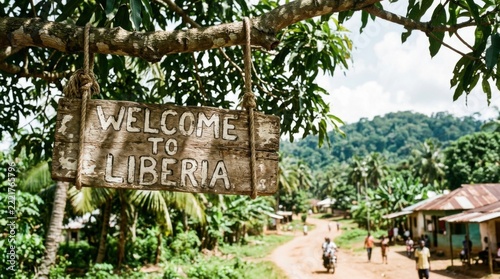 Welcome to Liberia wooden sign hanging from tree branch rural African village scene with people and lush greenery
