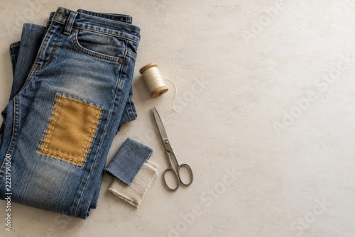 Patched Denim Jeans with Sewing Tools on Beige Background with Copy Space