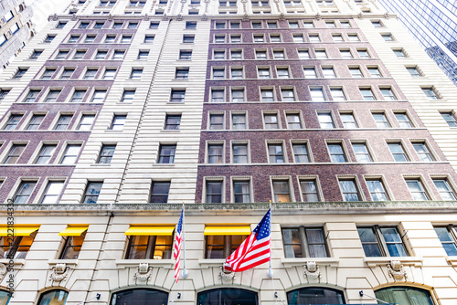 Low angle upward view of classic historic building facade decorated with waving American flags under blue sky