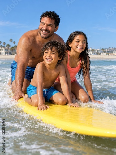 Smiling Father and Two Children on a Yellow Surfboard in Shallow Beach Waves