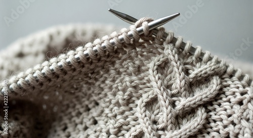 Knitting a cozy sweater with a cable knit pattern. Close-up of beige yarn and metal needles in a handmade craft project.