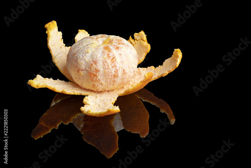 Peeled mandarin with curling citrus rind reflected on a glossy black surface