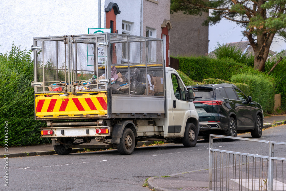 Fototapeta premium A specialized waste collection truck on the side of a residential road in the UK. A caged tipper truck, commonly referred to as a caged tipper van, a refuse collection van. A light commercial vehicle.
