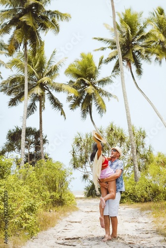 Happy young couple hug spin out of joy having fun together on sunny sandy pathway under tall coconut palm trees generic tropical island beach resort sunny summer day