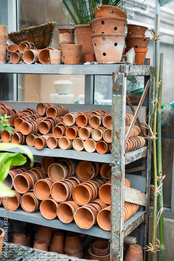 Naklejka premium Orangery supply and tools, terracotta flowerpots stacked on shelves of rack in greenhouse warehouse, empty ceramic pots organized on metal shelves in plant nursery room, horticulture and gardening.