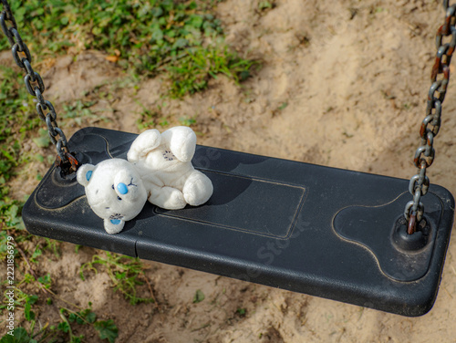 Lonely White Teddy Bear Left On Empty Playground Swing Suggesting Childhood Loss And Nostalgia