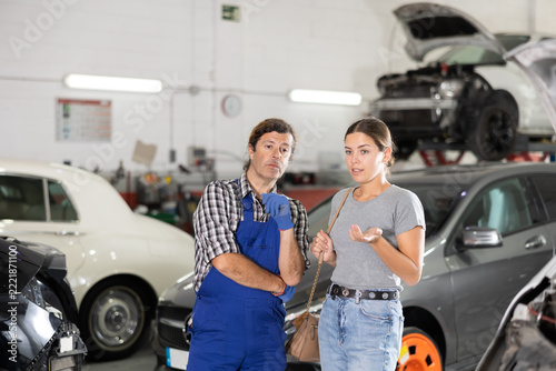 Expert mechanic providing detailed explanation to interested young female car owner regarding forthcoming repair of vehicle at auto service center