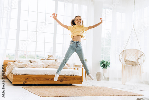 Young girl joyfully jumping in bright modern bedroom