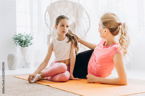 Mother and daughter bonding during home fitness exercise sitting on yoga mat talking