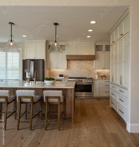 A spacious, upscale kitchen featuring a natural wood center island with white marble countertops and three cushioned bar stools.