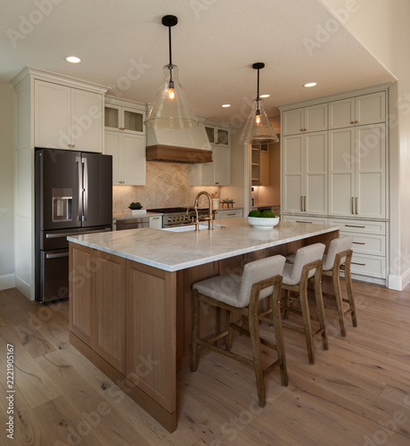A spacious, upscale kitchen featuring a natural wood center island with white marble countertops and three cushioned bar stools.