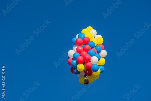 Cluster of colorful balloons lifting a small basket against blue sky
