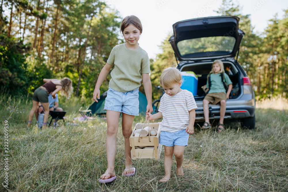 Fototapeta premium Siblings unloading luggage from car and setting up a campsite.
