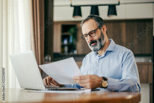 Mature man analyzing documents and working on laptop